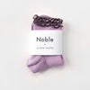 Purple socks with a brown ruffle edge on a white background, featuring 'Noble' and 'Le Bon Shoppe' labels.