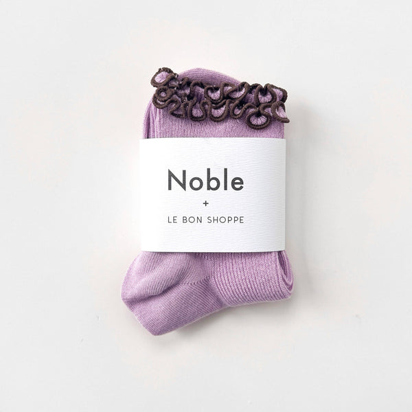 Purple socks with a brown ruffle edge on a white background, featuring 'Noble' and 'Le Bon Shoppe' labels.