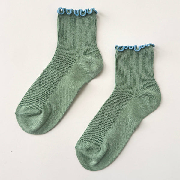 Pair of green socks with blue ruffle trim on a light gray background