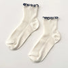 Soft white socks with navy ruffle edge on a neutral background.