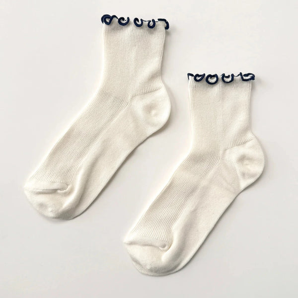 Soft white socks with navy ruffle edge on a neutral background.
