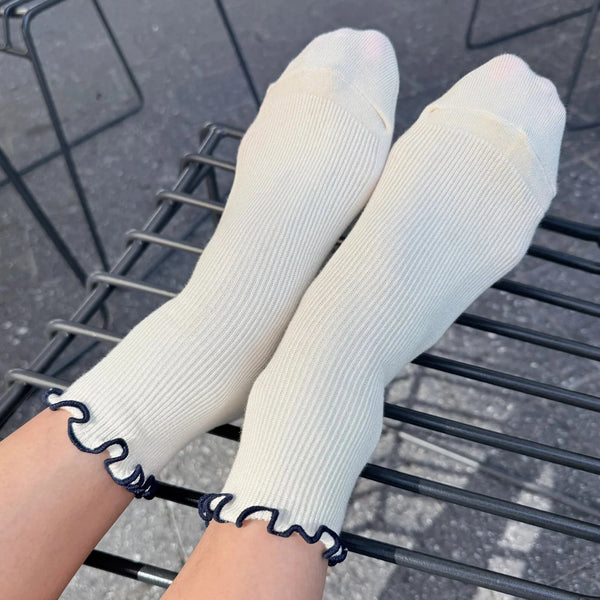 Person wearing white socks with navy ruffle edge against a dark outdoor backdrop.