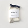White socks with navy ruffle edge in white paper branded packaging.