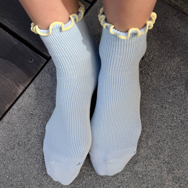 Light blue socks with ruffle yellow trim worn on a dark surface