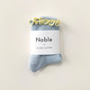 Blue socks with a 'Noble' + 'Le Bon Shoppe' label on a beige background