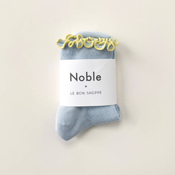 Blue socks with a 'Noble' + 'Le Bon Shoppe' label on a beige background
