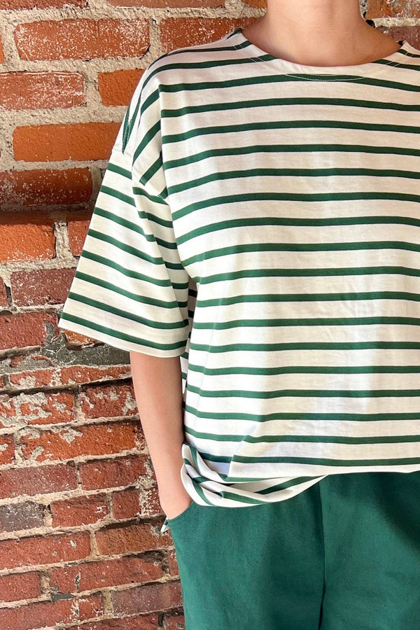 Person wearing a striped shirt and green shorts standing against a brick wall.