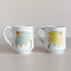 Two ceramic mugs with floral designs on a plain background