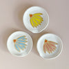 Three small ceramic spoon rests with coneflower designs in different colors.