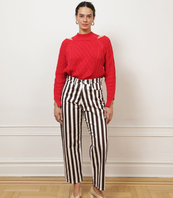 Woman wearing brown and white striped trousers against a white wall. 
