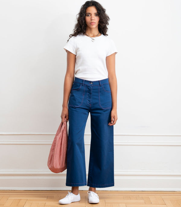 Person wearing dark blue wide leg pants against a white wall.