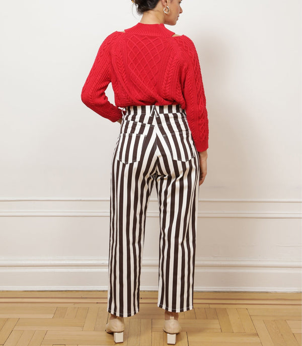 Person wearing brown and white striped trousers facing a white wall.