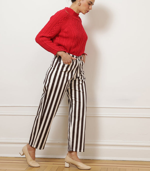 Person wearing brown and white striped trousers with hands in pockets against a white wall.
