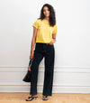 Woman wearing a yellow top and black high rise wide leg jeans holding a black handbag against a white wall.
