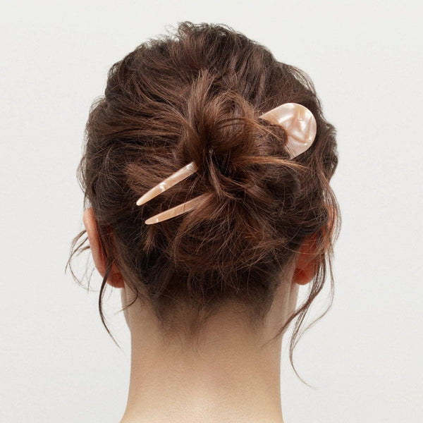Back view of a person with a stylish hair bun using hair pin on a plain background