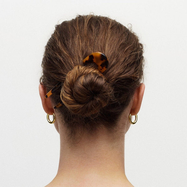 Back view of a person with a bun hairstyle featuring a tortoiseshell hair pin on a plain background