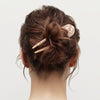 Back view of a person with a stylish hair bun using hair pin on a plain background