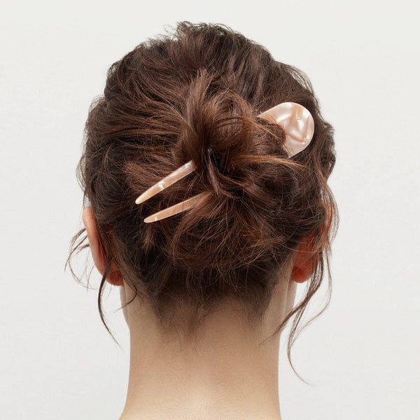 Back view of a person with a stylish hair bun using hair pin on a plain background