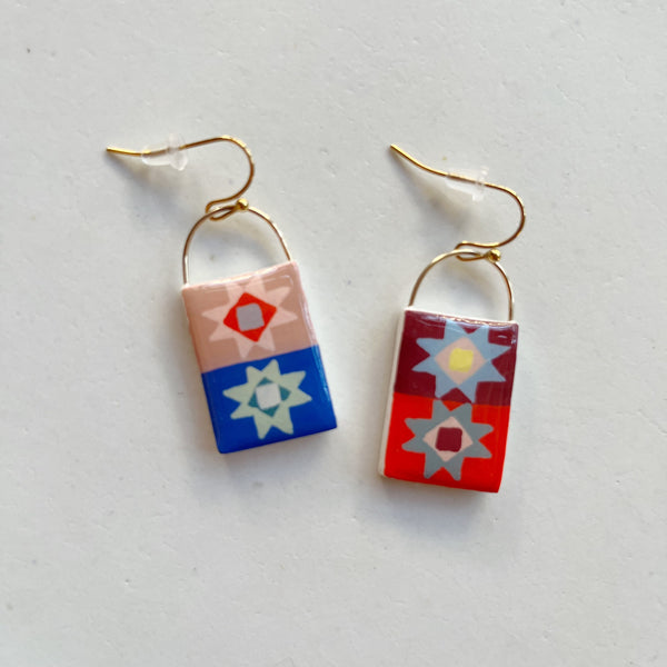 Glossy and colorful polymer clay earrings in a stacked quilt block design on gold hooks, against a neutral backdrop.