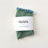 Green socks with blue ruffle edge in white paper branded packaging.