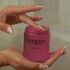 Hand holding a jar of Nopalera cactus body polish with a blurred background