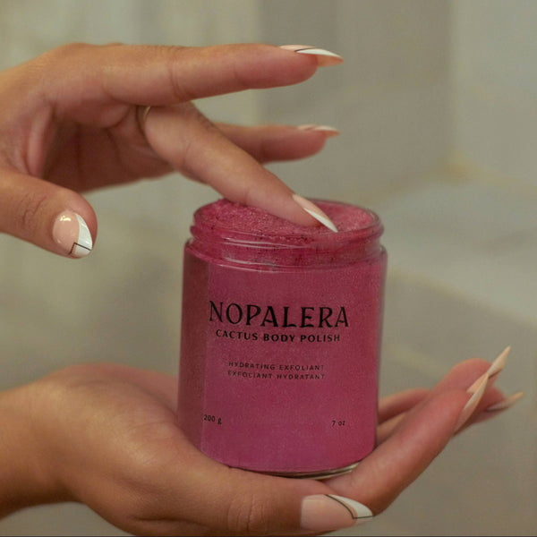 Hand holding a jar of Nopalera cactus body polish with a blurred background