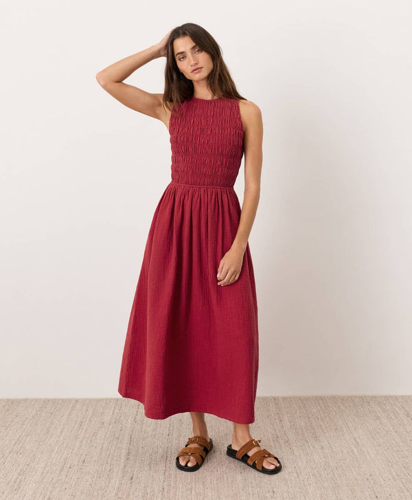 Woman wearing a red smocked bodice midi dress standing against a plain background