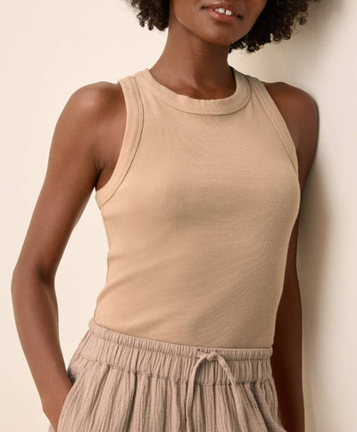 Woman wearing a beige sleeveless top and light-colored pants against a neutral background
