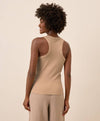 Woman wearing a beige racerback tank top and pants against a beige background