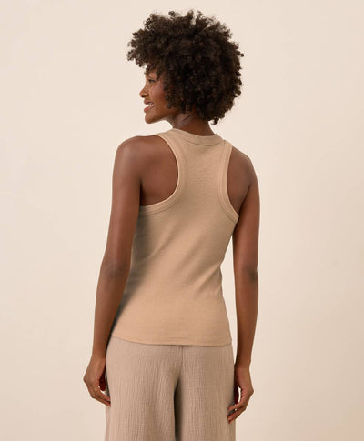 Woman wearing a beige racerback tank top and pants against a beige background