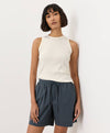 Woman wearing a cream-white sleeveless top and dark shorts against a light background