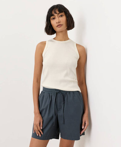 Woman wearing a cream-white sleeveless top and dark shorts against a light background