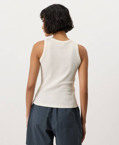 Person wearing a cream-white sleeveless top and dark pants on a light background