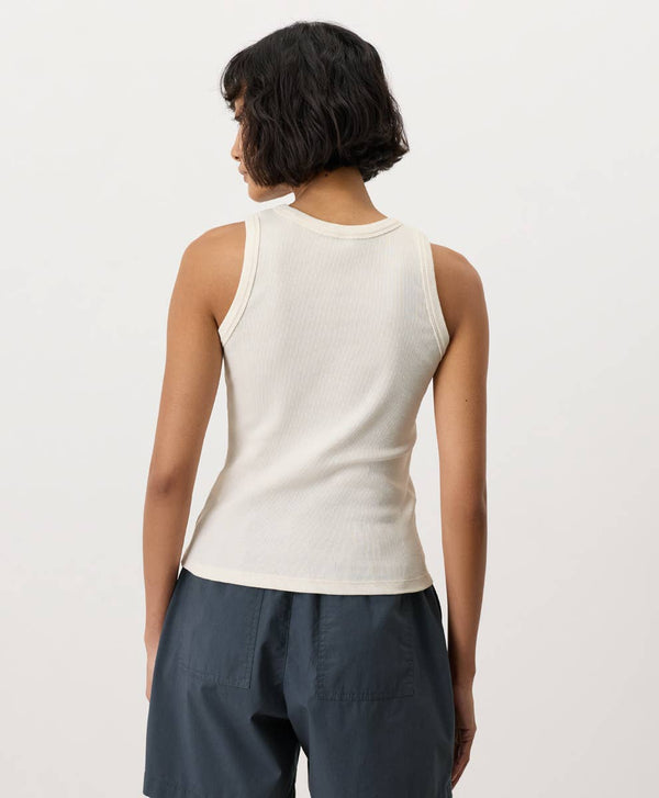 Person wearing a cream-white sleeveless top and dark pants on a light background