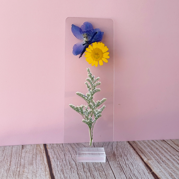 Pressed floral bookmark on a stand against a pink wall.