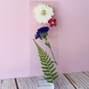 Pressed floral bookmark in a stand against a pink wall.