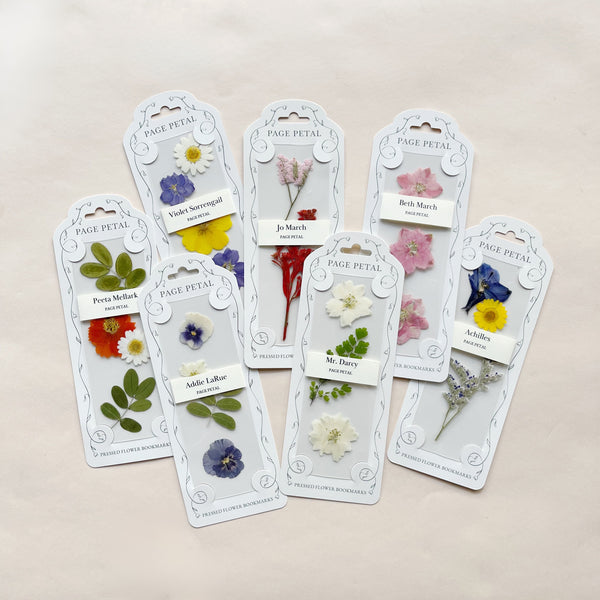 An assortment of pressed floral bookmarks in their packaging on a beige background.