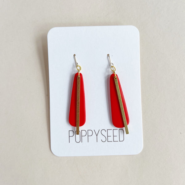 Red earrings with gold brass accents on a 'Poppyseed' branded card against a beige background