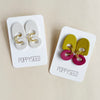 Two pairs of earrings on 'Poppyseed' branded cards against a beige background
