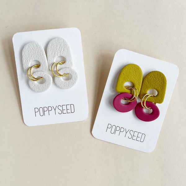 Two pairs of earrings on 'Poppyseed' branded cards against a beige background