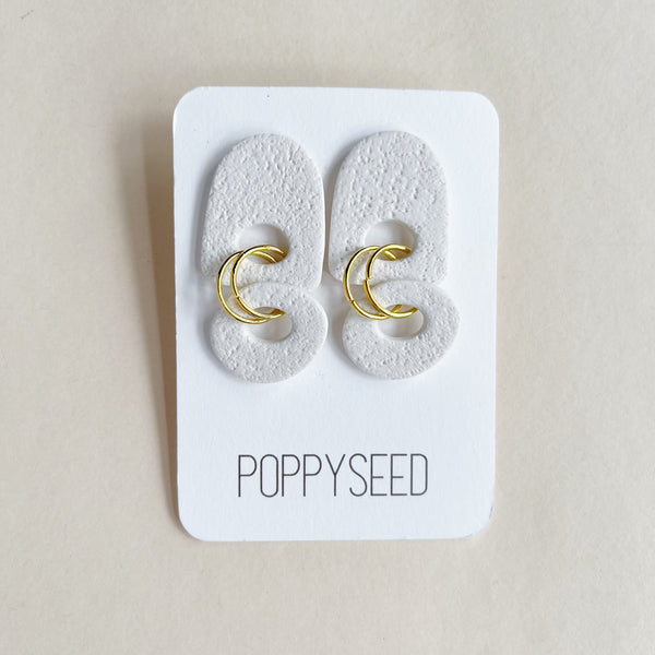 Textured white clay earrings with gold accents on a Poppyseed branded card against a beige background