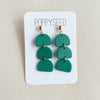 Green layered earrings on a Poppyseed branded card against a beige background