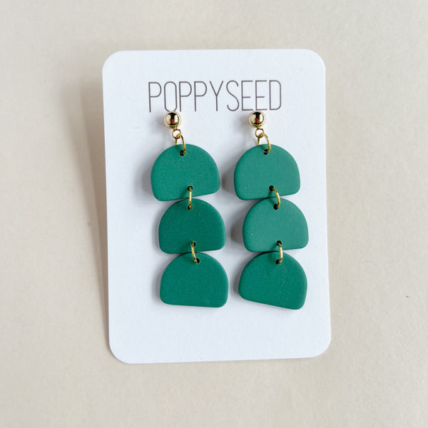Green layered earrings on a Poppyseed branded card against a beige background