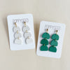 Two pairs of clay earrings on Poppyseed branded cards against a beige background