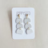 White layered earrings on a Poppyseed branded card against a beige background