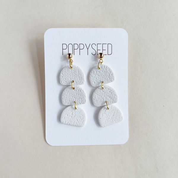 White layered earrings on a Poppyseed branded card against a beige background