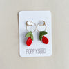 Pair of clay and gold hoop earrings on a 'Poppyseed' branded card against a beige background