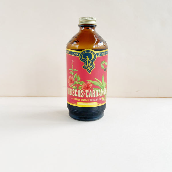 Bottle of Hibiscus Cardamom syrup with a colorful label on a white background