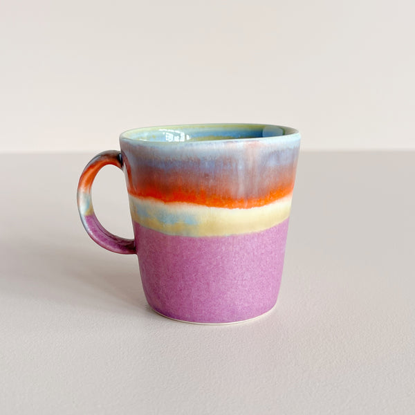 Multicolor glazed ceramic double espresso cup on neutral background.