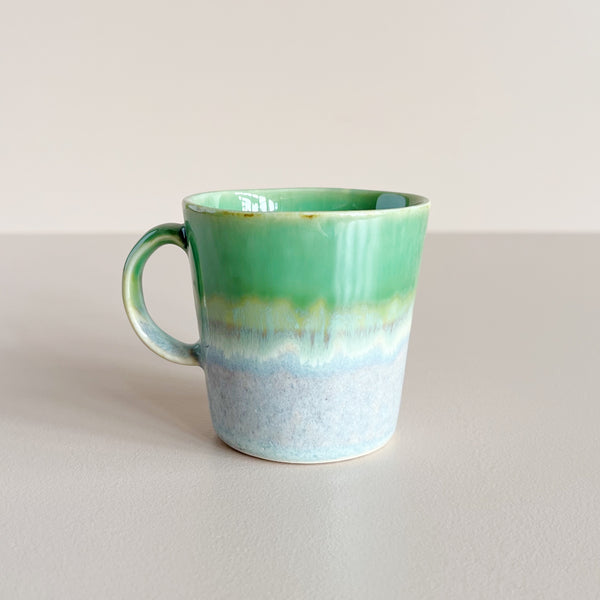 Green and speckled grey gradient glazed ceramic double espresso cup on neutral background.